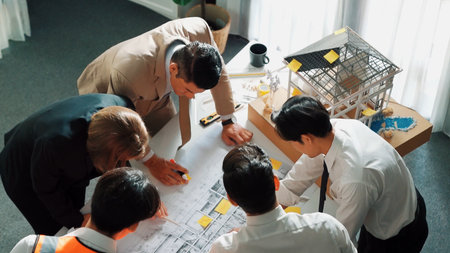 Top view of professional architect engineer team inspect house model while manager holding blueprint and asking about building construction. Group of diverse engineer working together.の写真素材