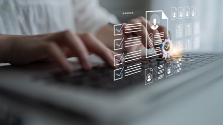 Close-up of hands typing on a laptop keyboard with a digital overlay showing checklists and user profile icons, symbolizing online assessment and productivity in a modern workspace.の写真素材