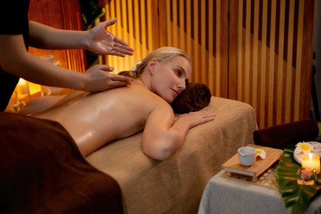 Caucasian woman customer enjoying relaxing anti-stress spa massage and pampering with beauty skin recreation leisure in warm candle lighting ambient salon spa at luxury resort or hotel. Quiescentの写真素材