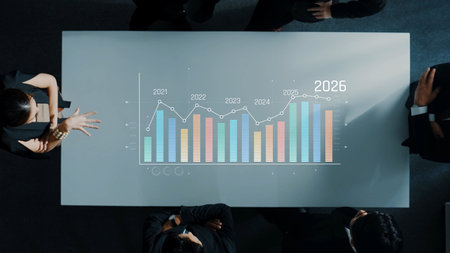 Aerial view of a business meeting showcasing colleagues discussing financial projections on a table featuring colorful graphs and data analytics for strategic decision-making. Rasterの写真素材