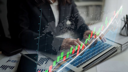 Businesswoman focused on analyzing financial data trends using a laptop, featuring graphical charts that signify growth in a modern office environment.の写真素材