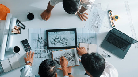 Top down view of professional manager looking at plan while designer holds blueprint while presenting project to smart team. Top aerial view of smart team planning building structure together.の写真素材
