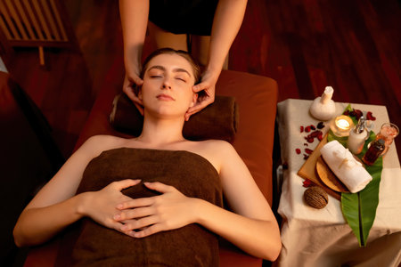Caucasian woman enjoying relaxing anti-stress head massage and pampering facial beauty skin recreation leisure in warm candle lighting ambient salon spa in luxury resort or hotel. Quiescentの写真素材