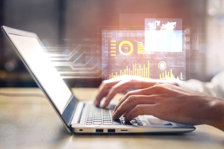 Professional setting featuring hands typing on a laptop with digital data visualization. Represents...