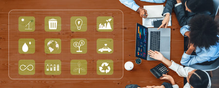 A diverse team of professionals gathers around a laptop, discussing sustainability strategies and...