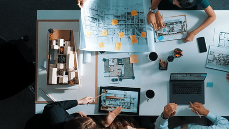 Top aerial view business people brainstorming about building interior at table with house model and laptop displayed house plan while architect engineer drawing and writing at blueprint.の写真素材