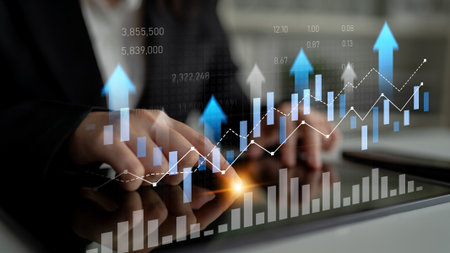 Business professional interacts with digital graphs and charts on tablet, showcasing financial trends and market growth in contemporary workspace setting.の写真素材