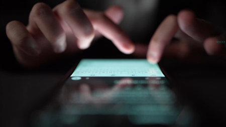 A close-up image showcasing hands typing on a smartphone screen illuminated by soft backlight at night, capturing the essence of modern digital communication and interaction.の写真素材