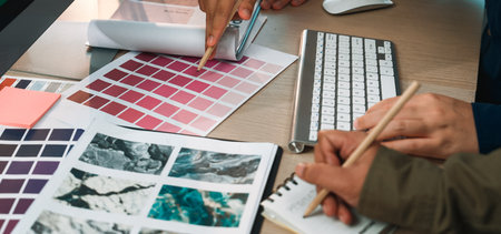 Two designers collaborate over color palettes, sketches, and digital tools, showcasing a creative workspace filled with inspiration for art and design projects.の写真素材