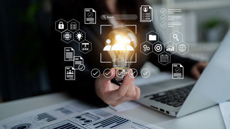 A business professional holds a glowing light bulb, surrounded by icons representing data and analytics, signifying innovative ideas and strategic planning in a modern office environment.の写真素材