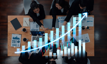 A business team engages in a meeting surrounded by charts and laptops, illustrating growth and strategy in a modern office environment focused on collaboration and data analysis.の写真素材