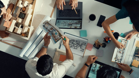 Architect team discussing and pointing and presenting blueprint to interior designer. Aerial view professional business people brainstorming building interior at table with house model.の写真素材