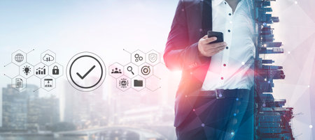 A modern businessman in a suit stands confidently, using his smartphone against a futuristic city backdrop filled with technology and communication icons.の写真素材