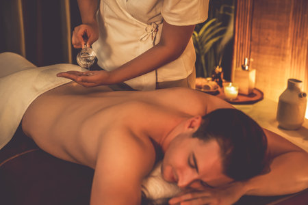 Masseur hands pouring aroma oil on man back. Masseuse prepare oil massage procedure for customer at spa salon in luxury resort. Aroma oil body massage therapy concept. Quiescentの写真素材