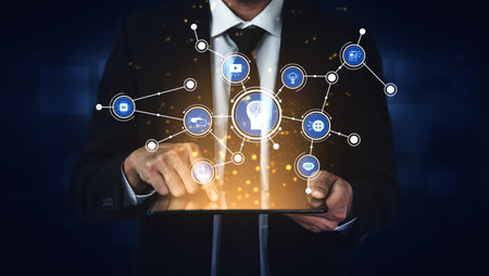 A businessman interacts with a tablet, accessing a digital network of virtual icons. This image...