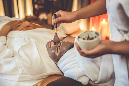 Serene ambiance of spa salon, woman customer indulges in rejuvenating with charcoal face cream massage with warm lighting candle. Facial skin treatment and beauty care concept. Quiescentの写真素材