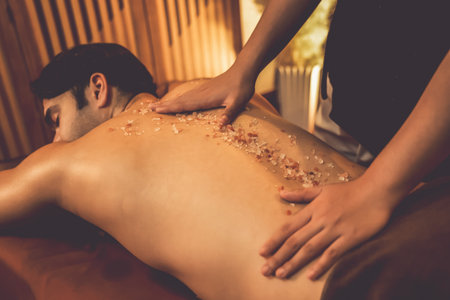 Man customer having exfoliation treatment in luxury spa salon with warmth candle light ambient. Salt scrub beauty treatment in Health spa body scrub. Quiescentの写真素材