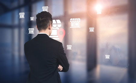 A focused businessman analyzes a digital map displaying store icons and a location pin, representing modern business strategy and data-driven decision making in an advanced office environment.の写真素材