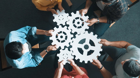 Top view of smart business people joining and gathering white gear together. Aerial view of diverse...