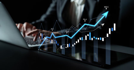 A business professional works on a laptop, analyzing financial data with emerging graphs to...