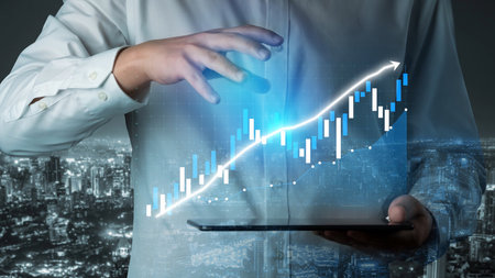 A businessman holding a tablet examines stock market trends with digital data visualization, reflecting professional analysis and ambition in a vibrant urban setting.の写真素材