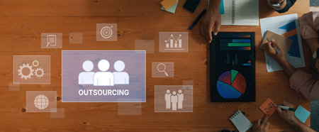 Aerial view of a wooden desk showcasing a collaborative outsourcing strategy with digital elements, charts, and diverse working tools creating a productive workspace.の写真素材