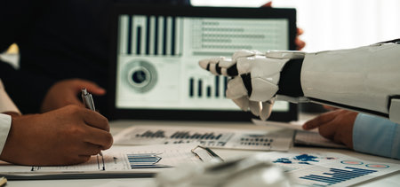 A dynamic business meeting showcases a robot assistant engaging with professionals in a modern office, presenting detailed data analysis and reports effectively.の写真素材