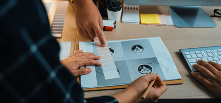 A detailed view of a collaborative design session in a modern office. Hands engage with sketches and color palettes, illustrating creativity and teamwork in a workspace.の写真素材
