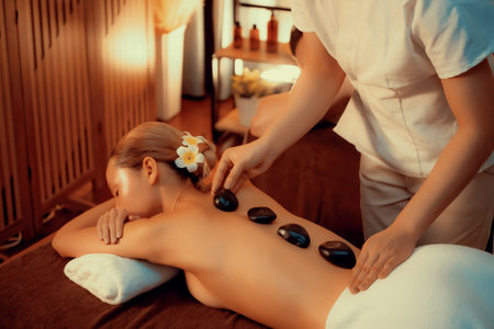 Hot stone massage at spa salon in luxury resort with warm candle light, blissful woman customer enjoying spa basalt stone massage glide over body with soothing warmth. Quiescentの写真素材