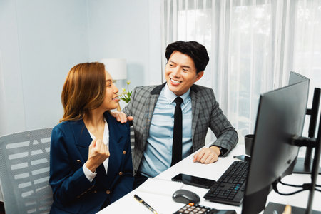 Successful smiling Asian business partners raising fist up together in profitable project job in stock exchange database on pc wearing formal suit at modern home office at side view image.の写真素材