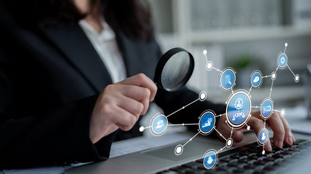 A business professional uses a magnifying glass to examine data analytics and customer relations, showcasing a modern office environment focused on technology and insight.の写真素材