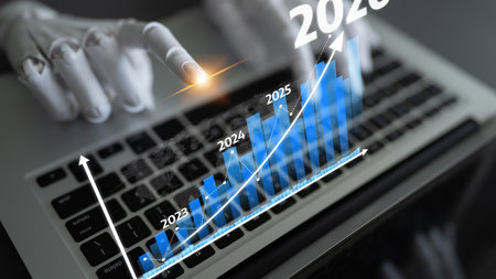 A robotic hand points at a digital graph on a laptop, illustrating growth and advancement in...