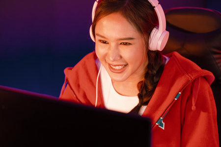 Portrait of Asian girl streamer playing online game wearing headphones talking with viewers media...
