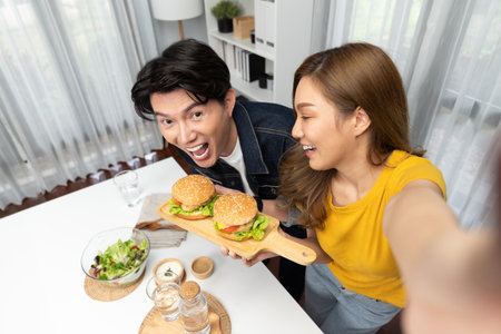 Top view of smiling host chef influencers taking photo with smartphone by selfie holding double hamburger on cooking show special easy with salad side dish homemade on social media channel.の写真素材
