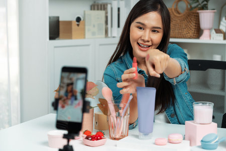 Young beautiful Asian showing cosmetic makeup lipstick matte pastel color testing on arm test promotion on social media online recording smartphone at modern room.の写真素材