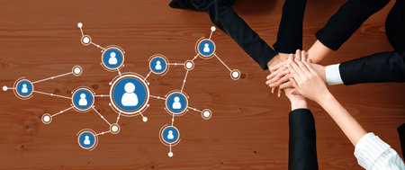 Hands unite on a wooden table with an overlaid graphic of human connections, symbolizing teamwork in...