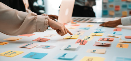 A diverse group of professionals engages in a vibrant brainstorming session, surrounded by colorful sticky notes on a table, showcasing teamwork and idea generation.の写真素材