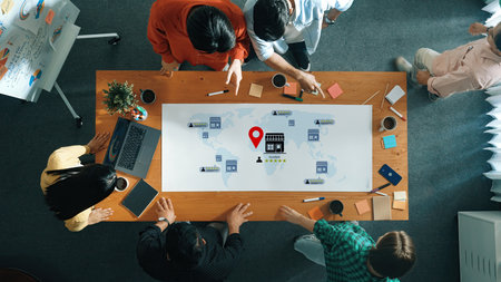 Engaged professionals collaborate around a table, analyzing a world map with icons, focusing on...