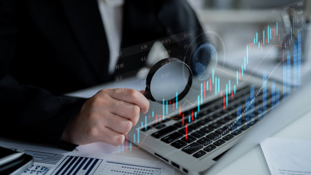 A business professional uses a magnifying glass to analyze stock market data on a laptop, highlighting the importance of detailed financial analysis and investment decisions.の写真素材