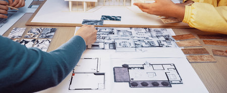 A vibrant workspace featuring a collaborative design session focused on modern architecture, showcasing plans, materials, and sketches on a central table.の写真素材