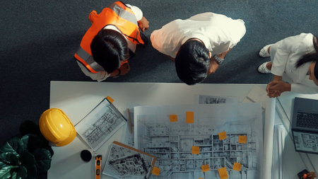 Top down view of project manager shaking hand with civil engineer at meeting table with blueprint...