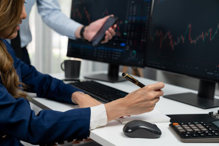 Cropped hand of businessman showing dynamic stock market data on phone to woman writing to memo for...