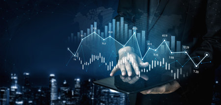 A business professional interacts with a digital tablet while analyzing stock market trends. The...