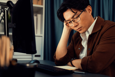 Businessman with stressful face working on pc to create business plan report over late night time at...