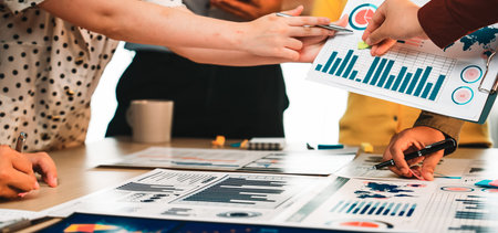 A diverse group collaborates over various data charts and graphs in a modern office workspace,...