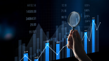 A hand holding a magnifying glass examines a financial chart displaying upward trends and blue bars,...