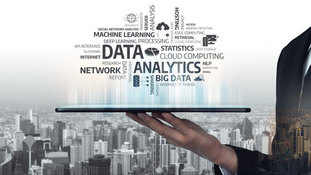 A businessman holds a tablet displaying a cloud of keywords related to data analytics, surrounded by...