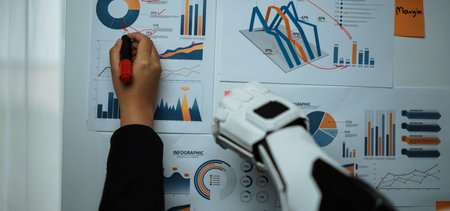 A robot arm and a human hand collaboratively review business infographics on a wall, showcasing...