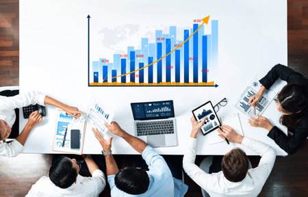 A diverse business team collaborates around a modern table, analyzing a financial growth chart on...