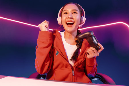 Host channel of smiling beautiful Asian girl streamer with joystick playing with raising fist up...